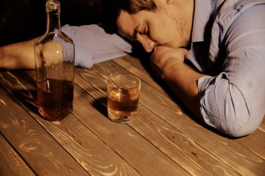 Alkolik bağımlısı. Masanın yanında alkollü ve bardaklı bir adam var. Tehlikeli bir alışkanlık. Sağlıksız yaşam konsepti. Sosyal sorun.