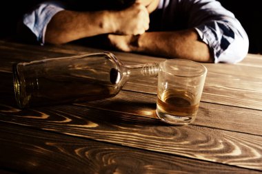 Alkolik bağımlısı. Masanın yanında boş şişesi ve bardağı olan bir adam var. Tehlikeli bir alışkanlık. Sağlıksız yaşam konsepti. Sosyal sorun.