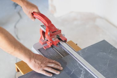 Bir işçi özel bir testere makinesinin seramik fayansını kesiyor. Dairede bakım onarımı var. Yenileme işlemi.