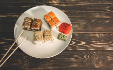 Ahşap arka planda yemek çubukları olan tabakta suşi. Japon usulü akşam yemeği. Sağlıklı gıda konsepti. Somon, wasabi ve zencefil. Vejetaryen.