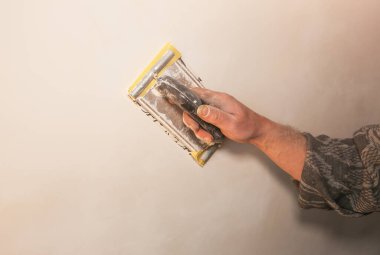 Adam zımpara kağıdıyla bir yüzeyi hazırlıyor. Duvar gıcırtısı. Bakım onarımı dairede tadilat yapıyor. Kapalı alanda restorasyon. Somut arkaplan.