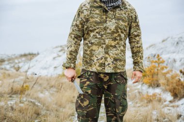 Asker kamuflaj üniforması içinde ve damalı keffiyeh shemagh bandanası içinde duruyor. Terk edilmiş bir yerde bıçaklı bir terörist var. Savaş konsepti.