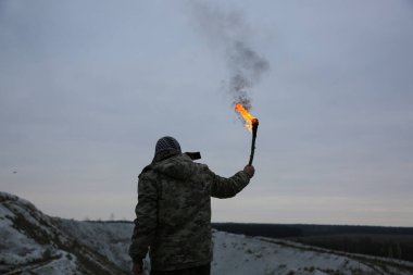 Asker meşaleyi ateşle tutuyor. Kamuflaj üniformalı ve damalı keffiyeh shemagh bandana giyen adam. Dağlardaki teröristler tıka basa doydu. Savaş konsepti. Beyaz tepeler ve çöldeki kuru otlar..