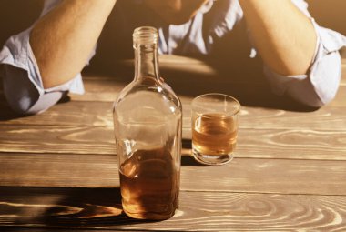 Alkolik bağımlısı. Masanın yanında alkollü ve bardaklı bir adam var. Tehlikeli bir alışkanlık. Sağlıksız yaşam konsepti. Sosyal sorun.