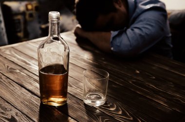 Alkolik bağımlısı. Masanın yanında alkollü ve bardaklı bir adam var. Tehlikeli bir alışkanlık. Sağlıksız yaşam konsepti. Sosyal sorun.