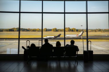 KATOWICE HAVAALANI, POLAND - 15 Ekim 2018: Havaalanında bavullarıyla oturan turistler. İnsanlar uçuşu bekliyor. Seyahat konsepti fotoğrafı. Gecikmiş uçak.