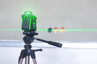 Üç ayaklıdaki lazer bina seviyesi duvarda parlıyor..