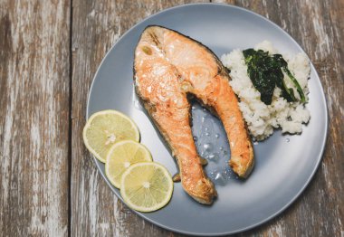Gri ahşap arka planda ıspanaklı ve limonlu gri tabakta ızgara somon balığı bifteği. Omega 3 vitamini, sağlıklı yaşam tarzı. Doğal vejetaryen yemekleri. Üst görünüm.
