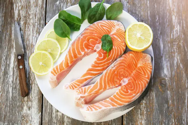 Ispanak ve limonlu, gri ahşap arka planda beyaz bir tabakta iki parça taze somon bifteği. Omega 3 vitamini, sağlıklı yaşam tarzı. Doğal vejetaryen yemekleri. Üst görünüm.