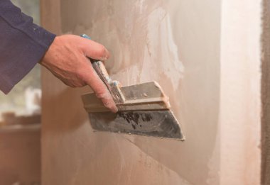 Adam palet bıçağıyla yüzeyi kaplıyor. Bakım onarımı dairede tadilat yapıyor. Kapalı alanda restorasyon. Somut arkaplan.