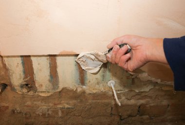 Adam palet bıçağıyla yüzeyi kaplıyor. Bakım onarımı dairede tadilat yapıyor. Kapalı alanda restorasyon. Somut arkaplan.