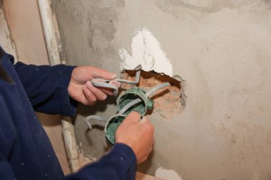 İnsanlar elektrik üretiyor. Bakım onarımı dairede tadilat yapıyor. Kapalı alanda restorasyon. Duvardaki deliklerde soket anahtarları için renkli kablolar var..