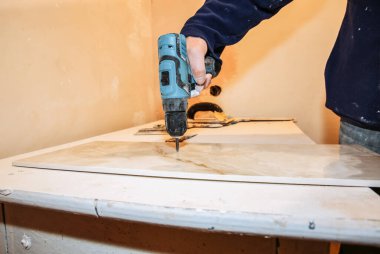 İşçi elinde elektrikli matkap ve apartmandaki panelleri kesiyor. Bakım onarımı, parşömen testeresiyle dairede tadilat yapıyor. Kapalı alandaki fayansların restorasyonu.