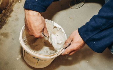 Adam kovada macun macununu karıştırıyor. Duvar gıcırtısı. Bakım onarımı dairede tadilat yapıyor. Kapalı alanda restorasyon. Somut arkaplan.