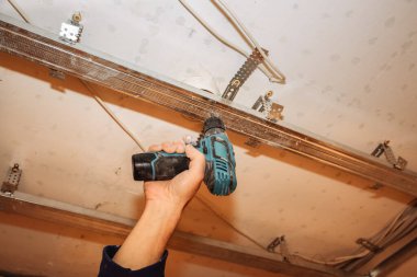 Gergin tavanlı metal yapılar. Elektrikli matkap kullanan bir adam. Bakım onarımı dairede tadilat yapıyor. Kapalı alanda restorasyon. Somut arkaplan.