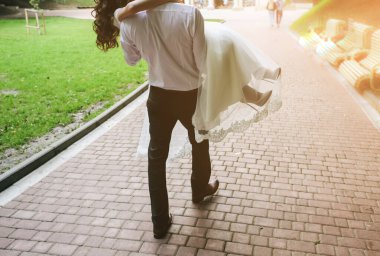 Damat gelini elinde tutuyor. Yeşil Park 'ta yürüyen güzel bir düğün çifti. Aşık gençler..