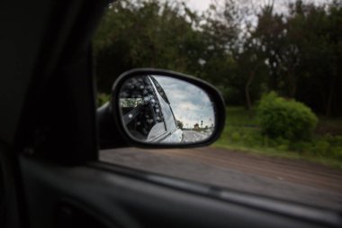 Dikiz aynasındaki yolun yansıması. Seyahat konsepti. Kötü hava ve gri gökyüzü.