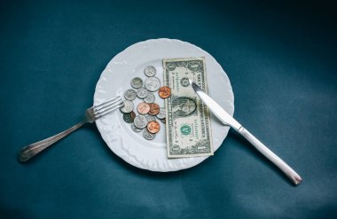 Çatal ve bıçakla tabakta bir dolar var. Para fotoğrafı yok. Fakirlerin fikri. Bozuk paralar. Küçük maaş ve emekli maaşı yiyecek için yeterli değil. Sosyal sorunlar.