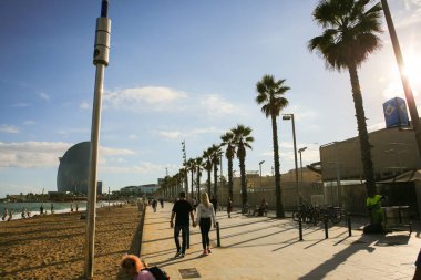 BARCELONA, İspanya - 15 Ekim 2018: insanlar Barcelona plajı boyunca yürüyorlar. İspanyol güneşli günü. Palmiye ağaçları.