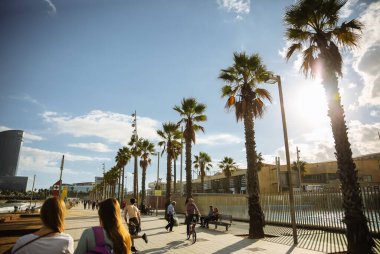 BARCELONA, İspanya - 15 Ekim 2018: insanlar Barcelona plajı boyunca yürüyorlar. İspanyol güneşli günü. Palmiye ağaçları.