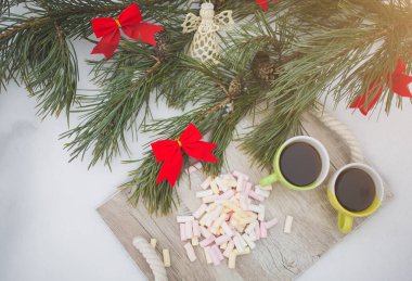 İki kahve fincanı ve marşmelov kış pikniğinde dışarıda yatıyor. Ormanda çam ağacı ve tahta tepsi. İyi tatiller. Noel süslemeleri. Romantik kutlama..