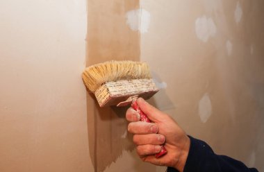 Adam bir fırçayla yüzeyi hazırlıyor. Bakım onarımı dairede tadilat yapıyor. Kapalı alanda restorasyon. Somut arkaplan.