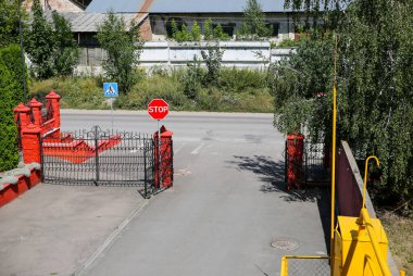 Sanayi bölgesi. Fabrika bölgesi. Açık havada yeşil ağaçlar. Yoldaki kırmızı dur işareti. Yaya bölgesi.