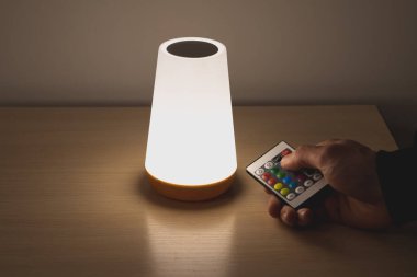 İnsanoğlu modern renk değiştiren lambayı ayarlıyor. Evdeki rahat atmosfer için uzaktan kumandalı eko şarj edilebilir başucu lambası..