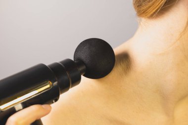 Kadın boynuna perküsyon masaj silahıyla masaj yapıyor. Fizyoterapi, kas düzeltme, kendine masaj aleti. Sağlık hizmetleri. Kapat..