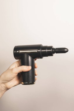Kadının perküsyon masaj tabancası tutarken çekilmiş dikey fotoğrafı. Vücudunun her yerinde küçük, düz bir başlık var. Fizyoterapi, kas düzeltme, kendine masaj aleti. Sağlık hizmetleri. Kapat..