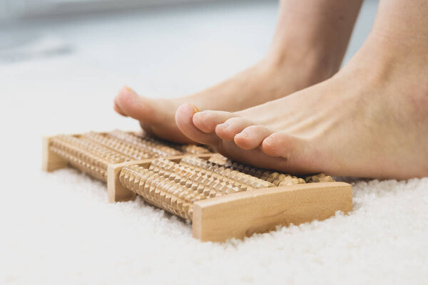 Woman massaging her feet with wooden roller foot massager. Self-massage for relaxing legs. Close up.