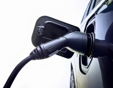 EV şarj prizi odaklı çekimde bulanık arkaplanlı elektrikli araca elle yerleştiriliyor