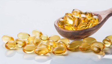 Altın sarısı haplar kaşıkta yere saçılmış. Yumuşak gıda takviyeleri, balık yağı, omega 3, D3 vitamini, E vitamini dolu kapsüller..