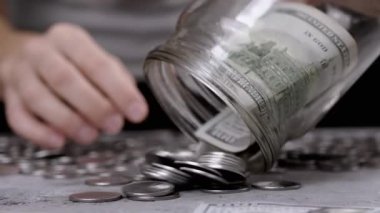 Kadın bozuk para ve 100 dolarlık banknotu cam kavanozdan masaya döker. Para sayıyorum. Beton zeminde bir sürü bozuk para var. Bütçe, harcama, tasarruf, birikim. Zenginlik, yoksulluk. Nakit.