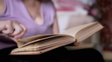 Kitap okuyan yaşlı bir kadın, Kapalı Kapılar 'daki güneş ışınlarında sayfaları çeviriyor. Yakın plan. Emeklinin biri elinde bir kitap tutuyor, okuyor ve emekliliğinde evde dinleniyor. Yaşlıların yaşam tarzı..