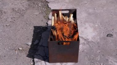 Açık havada dumanlı odun sobasında parlak bir alevle doğranmış odun yanığı. Kızgın kırmızı bir şenlik ateşi, durgun bir ızgarada, güneş ışığının arka bahçesinde beton asfalt üzerinde duruyor..