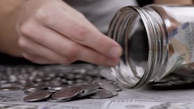 Cam kavanozu gümüş para ve 100 dolarlık banknotlarla dolduran kadın. Domuz kumbarası. Beton zeminde Ukrayna sentleri ve nakit para yatıyor. Bütçe, ödeme, harcamalar, tasarruflar. Finansal kriz. Stok.