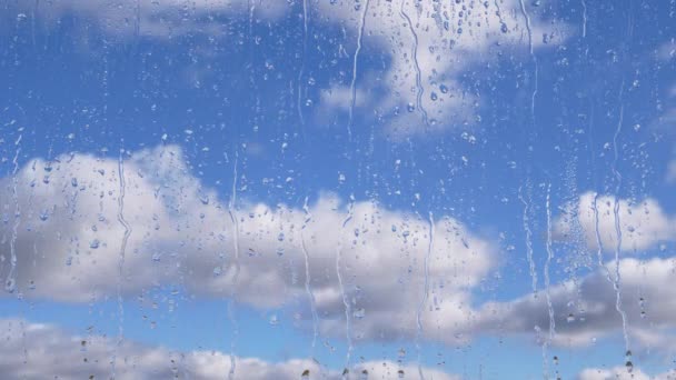 雨滴が移動雲と青空の背景を背景にガラスを流れ落ちる 時間の経過 高速で移動する積雲 雨の日だ 水のストリームは ガラス上のウィンドウを流れる 気象学 — ストック動画