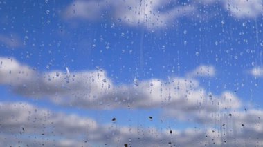 Yağmur Damlaları, Hareket Eden Bulutlar ve Mavi Gök 'ün Arkaplanına Karşı Camdan Aşağı Akıyor. Yavaş çekim. Kümülüs bulutları hareket ediyor. Yağmurlu bir hava. Camdaki sisli su akıntıları pencereden aşağı akıyor. Meteoroloji.