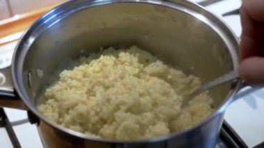 Şef Millet lapasını fırının üstünde kaşıkla tepside karıştırıyor. - Ne? Ev mutfağı. Sağlıklı yemek buharı. Tencerede sıcak yulaf lapası. Yakın plan. Sarı mısır gevreğinden akşam yemeği hazırlığı.