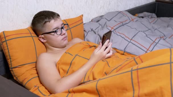 Adolescente Gafas Escribiendo Mensajes Texto Teléfono Inteligente Acostado Una Cama — Vídeo de stock