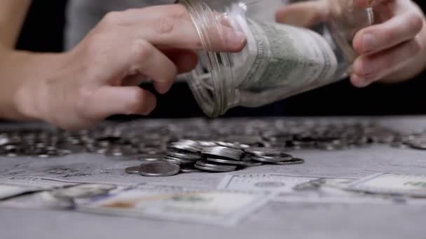 女士倒零钱和100美元的钞票从玻璃瓶放在桌上 许多硬币躺在混凝土的背景上 — 图库视频影像