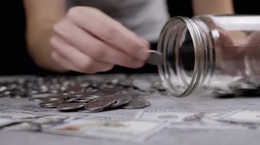 Cam Kavanozu Gümüş Paralarla Dolduran Kadın Masaya Dağılmış. Domuz kumbarası. Beton zeminde Ukrayna sentleri ve 100 dolarlık banknotlar yatıyor. Bütçe, ödeme, harcamalar, tasarruflar. Stok.