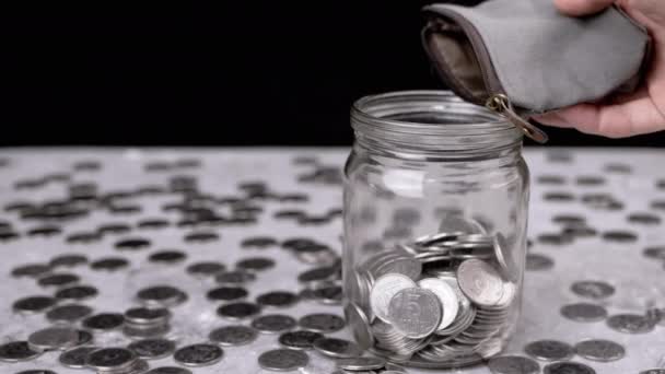 女人把零钱从钱包里倒进了皮吉银行的玻璃瓶里 散落的银乌克兰分币和便士放在桌子模糊的背景上 — 图库视频影像