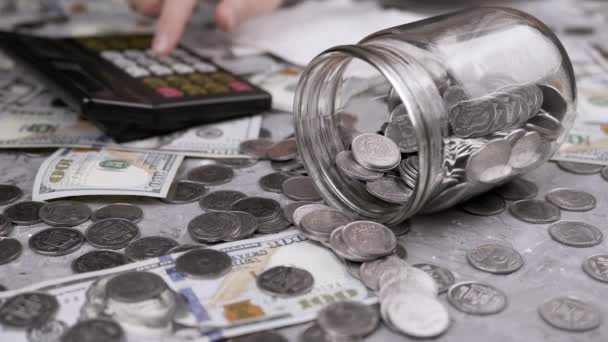 女人在带硬币的罐子前计算计算器上的花费 乌克兰元和100美元的钞票散落在桌上 金融危机 — 图库视频影像