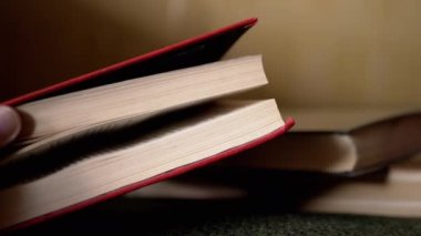Elleri Kalın Kırmızı Kitap Açar Bulanık Arkaplan 'a karşı çevirir. Bir kitabın sayfalarını çevirmek. Evde kitap okuyorum. Ev kütüphanesi. Gizemli bir atmosfer. Zayıf ışıklandırma. Bir yığın kitap. Yakın plan..