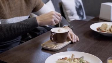 Erkek Elleri Kafe 'de bir çay kaşığıyla kalın köpük karıştırır. İnsan eli. Erkek, bir kafede ya da restoranda bir masada oturuyor. Köpük kapuçino kahvesi. Memnun oldum. Aroma.