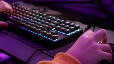 Hands Gamer sanal gerçeklik kulübündeki bir video oyununda RGB klavyesini çalıyor. Yakın plan. Hacker parmaklarıyla düğmelere basıyor, fareyi halının üzerinde hareket ettiriyor. Neon ışıkları. Kumar oynuyorum. ESports. VR.