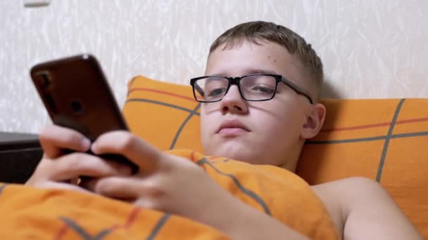 Tonåring Glasögon Skriva Textmeddelanden Smartphone Ligga Mysig Säng Trött Pojke — Stockvideo