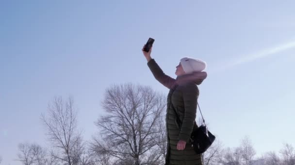 沮丧的女孩正试图在冬天的森林里抓住手机的信号 女人把智能手机伸向蓝天以寻找一个连接 冬日阳光明媚 无叶树 — 图库视频影像